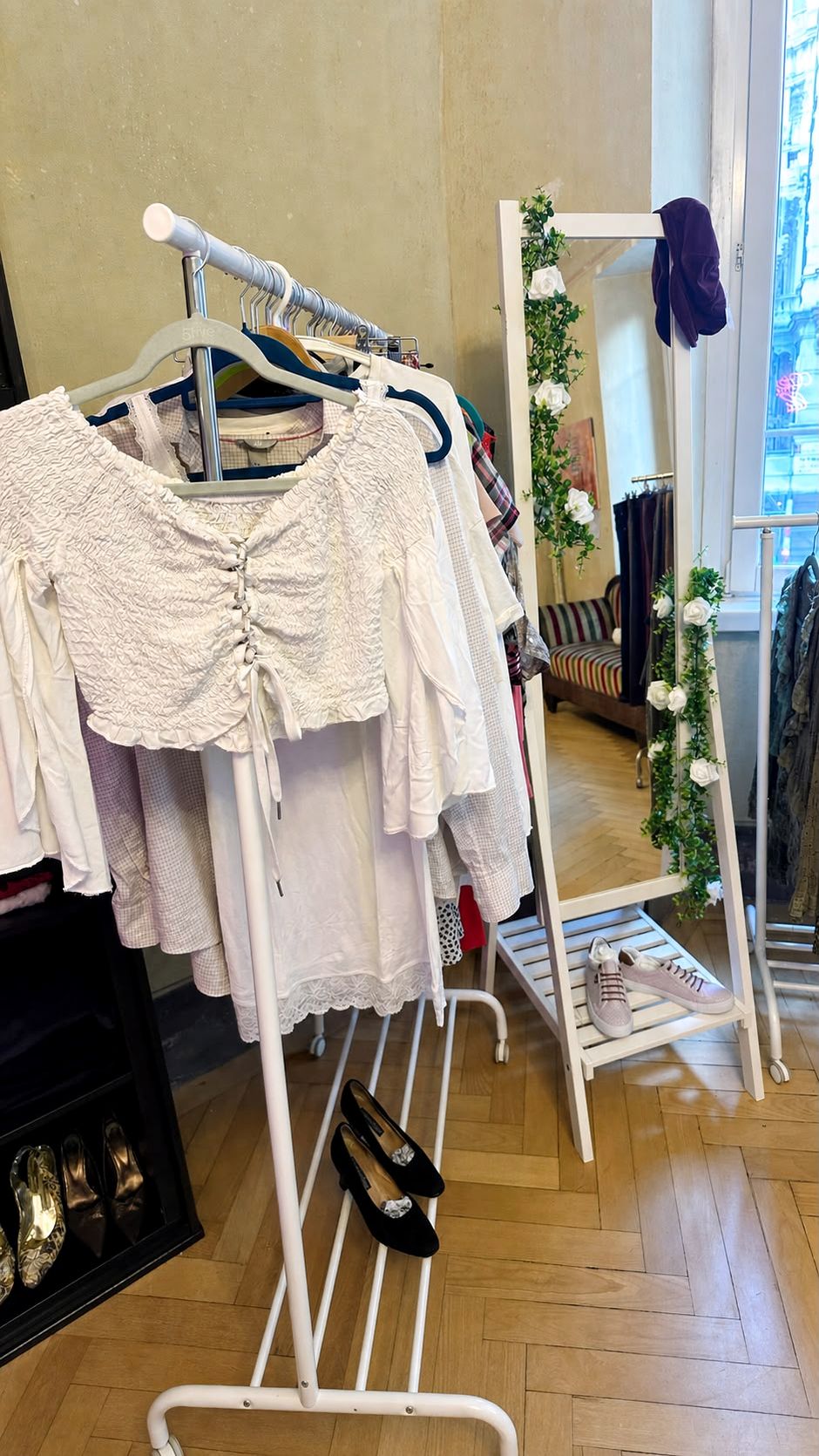 Capi chiari su una rella, accanto a uno specchio decorato con rose bianche nella boutique.
