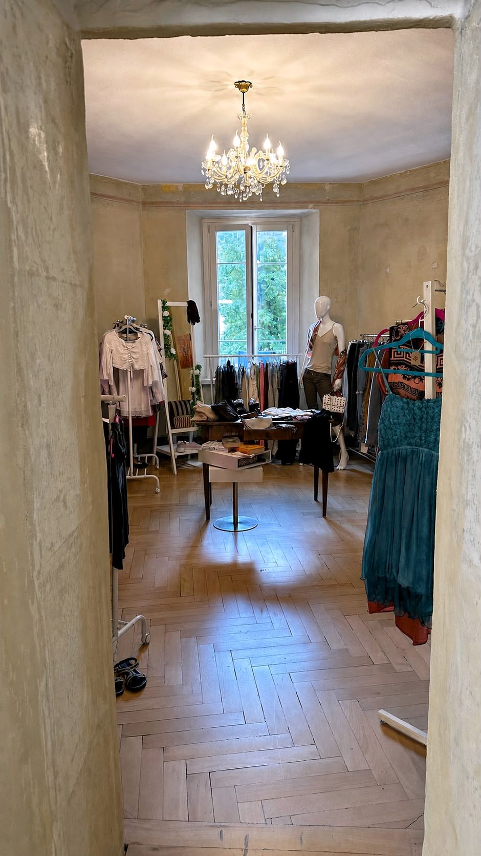 Uno sguardo nella boutique Autre Amour attraverso la porta, con lampadario, abiti e parquet.